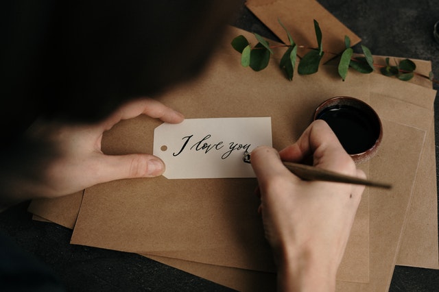 Jemand schreibt mit einem Tintenfüller auf eine kleine Karte "I love you"