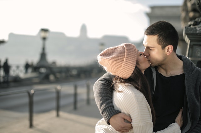 Ein junges Paar küsst sich vor einer Stadtkulisse.